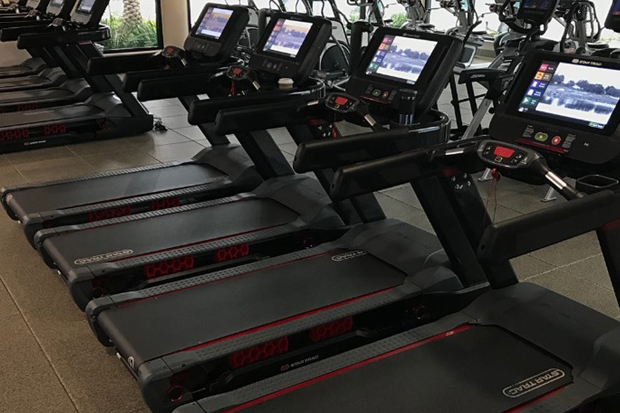 Row of black Star Trac treadmills with red accents and digital displays in gym facility