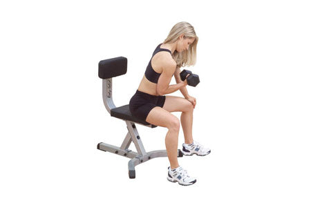Woman performing dumbbell exercise on gray and black utility bench with leg extension attachment