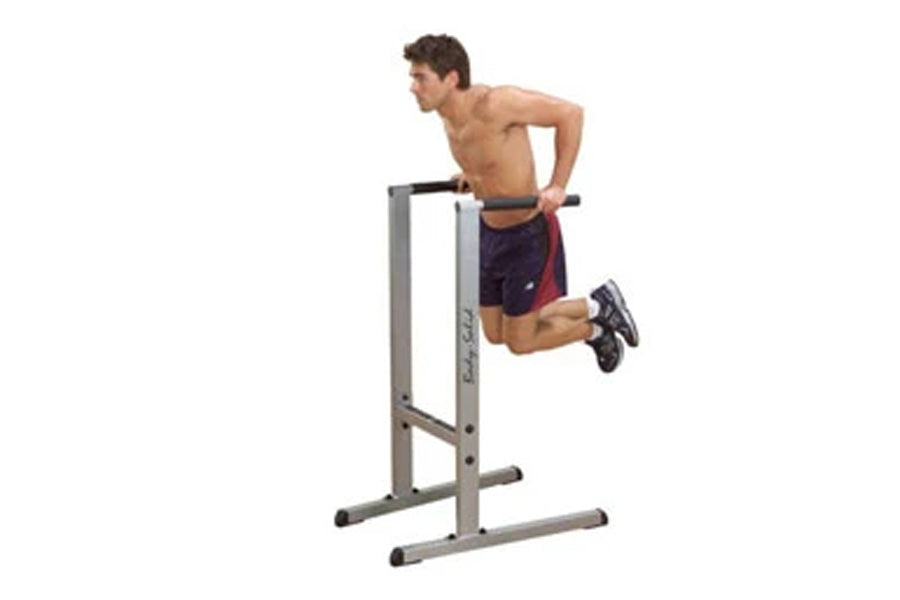 Man using gray and black Body-Solid dip station with horizontal bars, wearing navy shorts and black sneakers