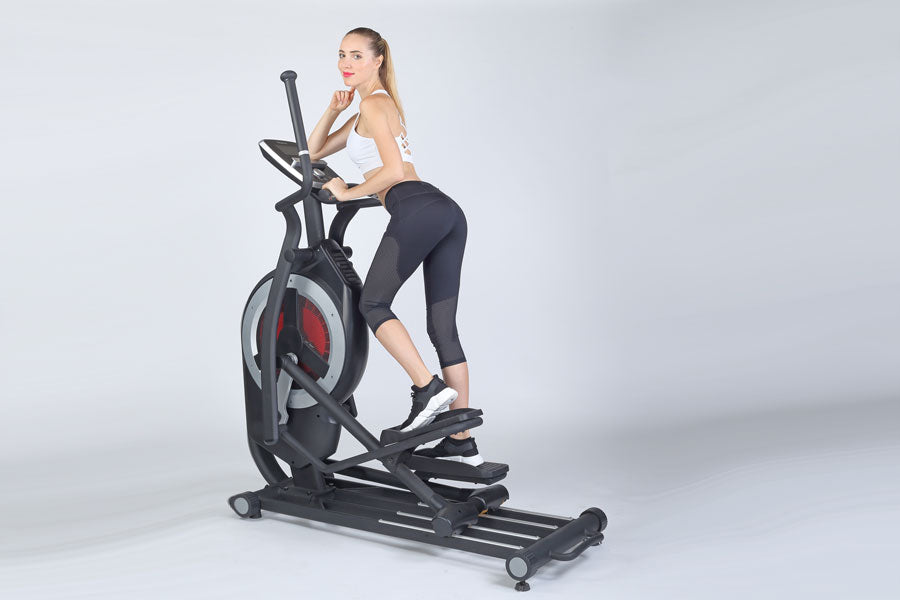 Woman using black elliptical machine with red wheel and digital display on white background