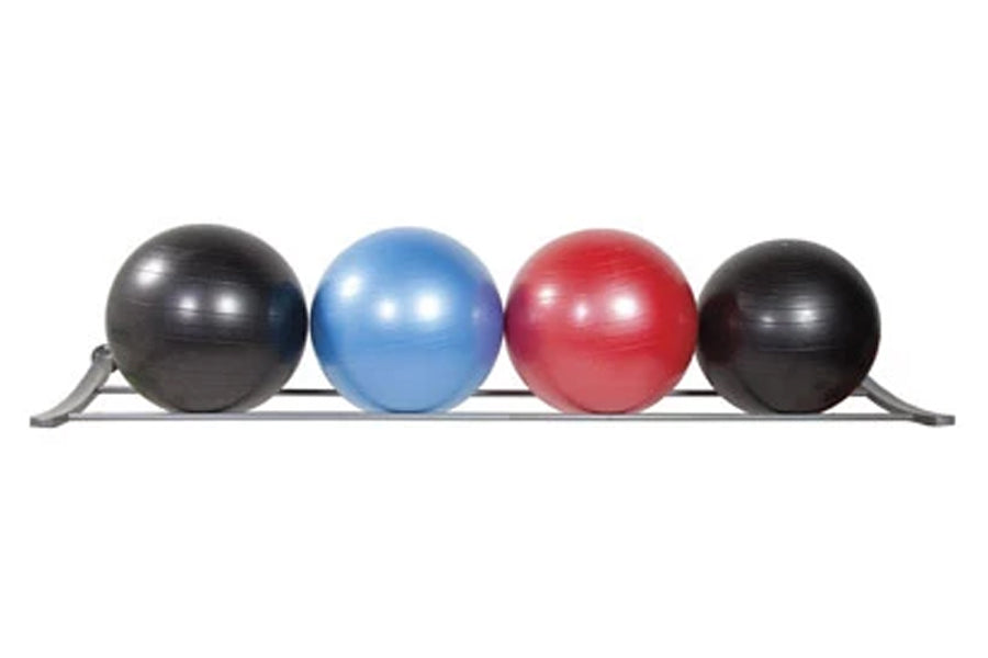 Four exercise stability balls in black, blue, red, and black resting on gray wall-mounted storage rack, white background