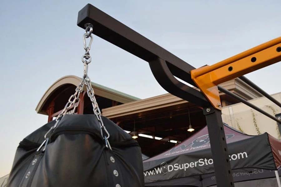 Black heavy bag suspended by silver chain from orange and black metal hoist arm apparatus