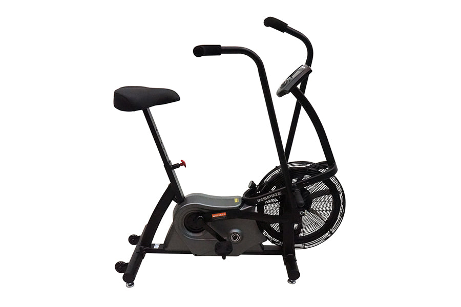Black upright air bike with padded seat, curved handlebars, large fan wheel, and digital display on white background