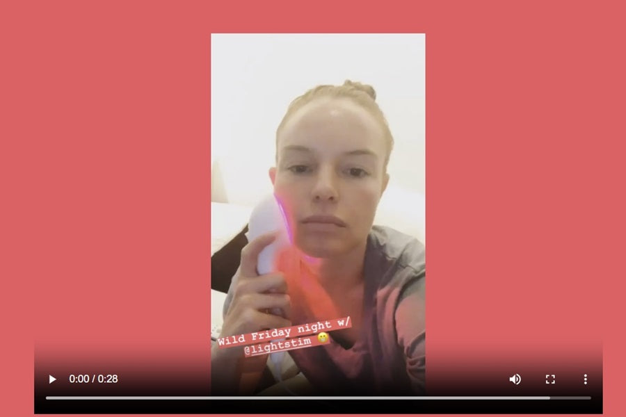 Person holding pink and orange LED light therapy device against face, demonstrating LightStim pain relief tool on white backg