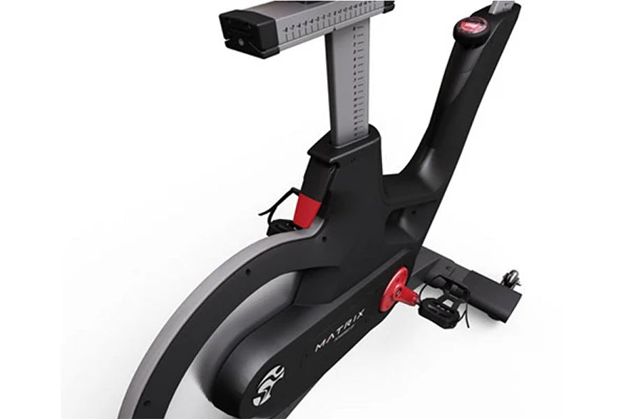 Matrix IC7 Indoor Club Group Cycle close-up of flywheel, red resistance knob, adjustable seat post, and SPD pedals