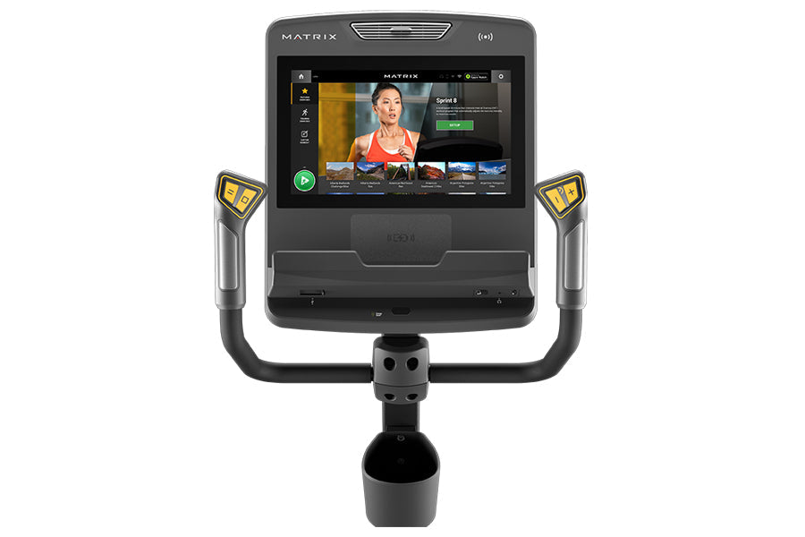 Matrix Performance Touch Hybrid Cycle with display screen showing fitness content, dual handlebar grips with yellow accent bu