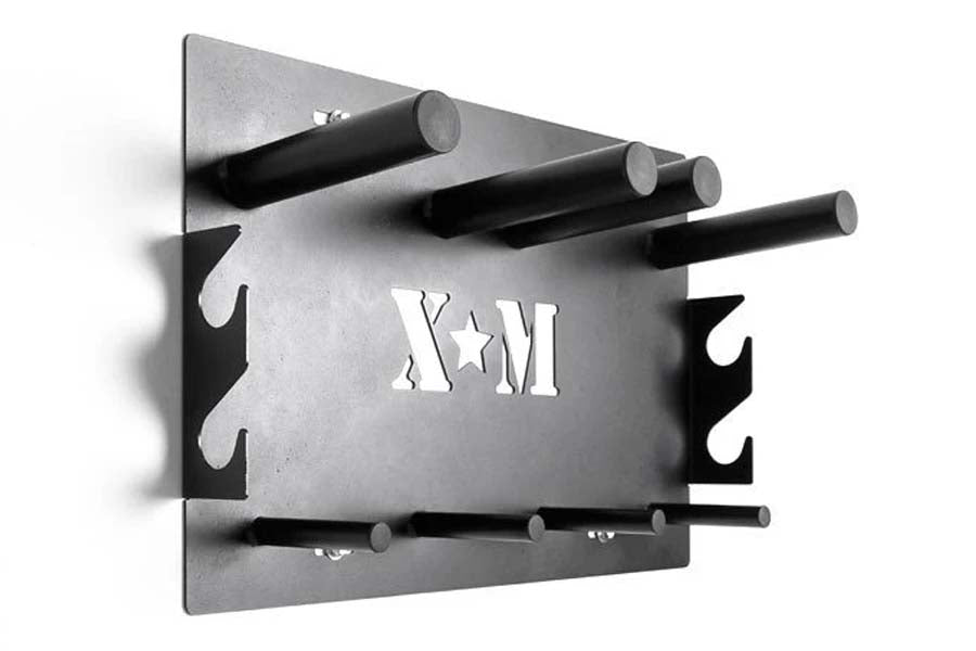 Wall-mounted weight plate storage rack in gray and black metal with multiple cylindrical pegs and "KAM" branding, flat lay vi
