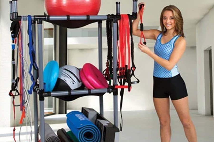 Black metal workout storage rack with two shelves holding red exercise ball, colored resistance bands, jump ropes, and yoga m