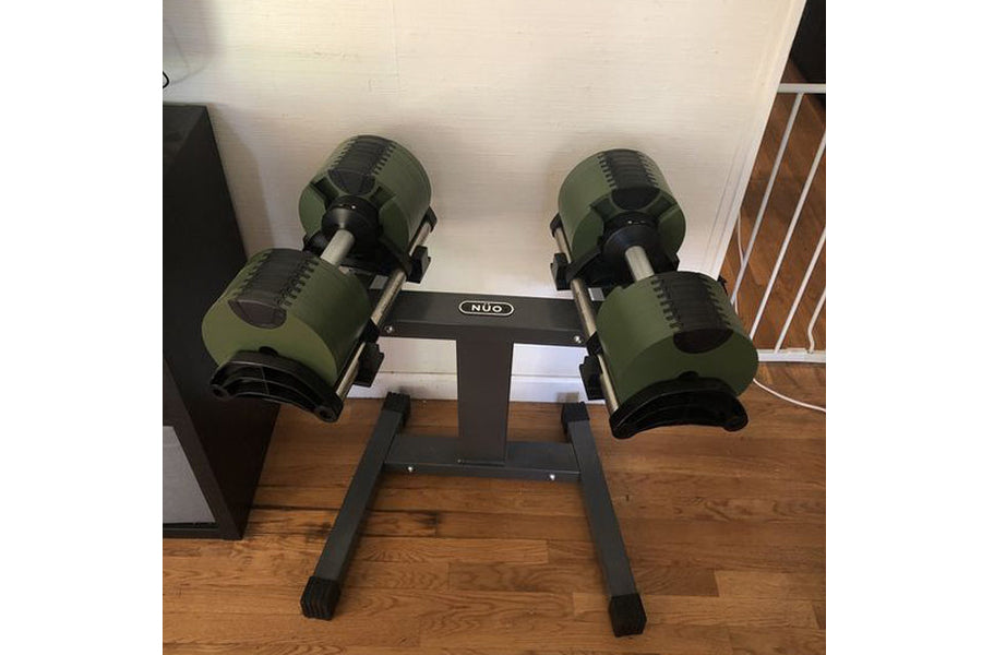 Pair of sage green adjustable dumbbells mounted on black single-legged stand with NUO branding, on wooden floor