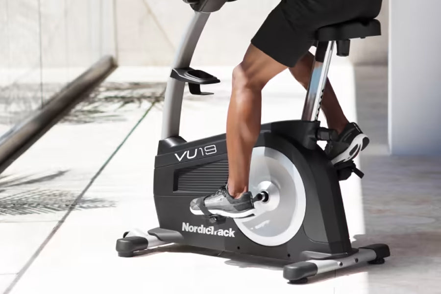 NordicTrack Commercial VU 19 upright exercise bike in black and white, worn by model in black workout clothes