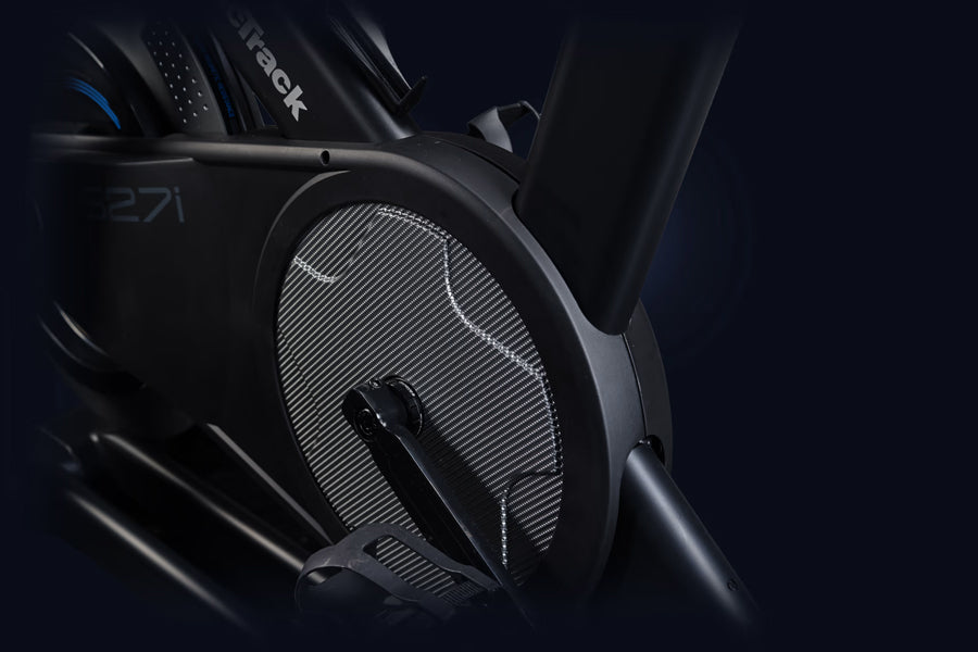 Black stationary exercise bike with ribbed flywheel and digital display on dark background