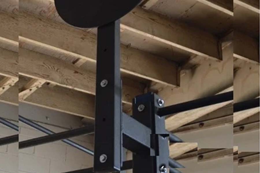Black metal wall ball target attachment mounted on power rack post with bolted bracket connection, showing exposed wood beam