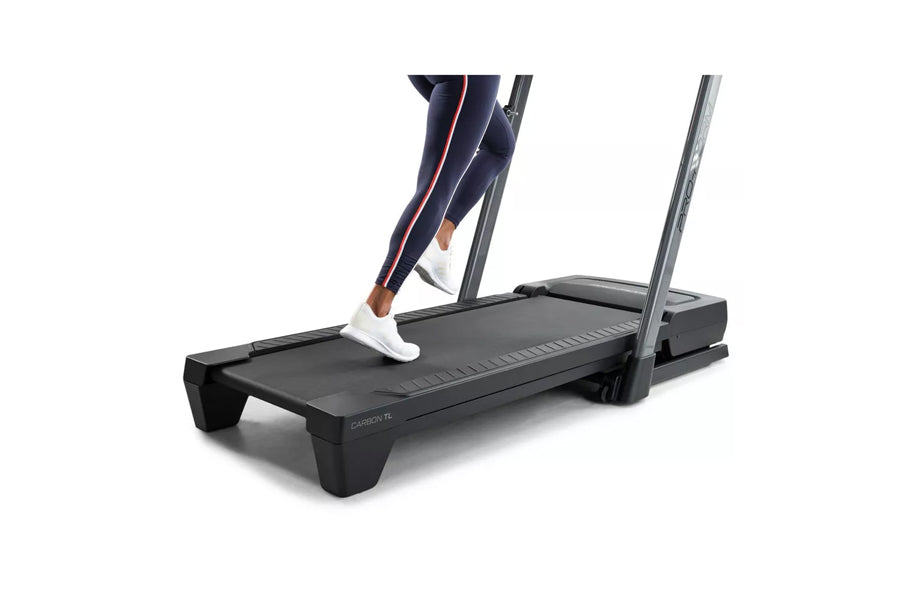 Black ProForm Carbon TL treadmill with gray uprights, person wearing navy leggings and white sneakers running on belt