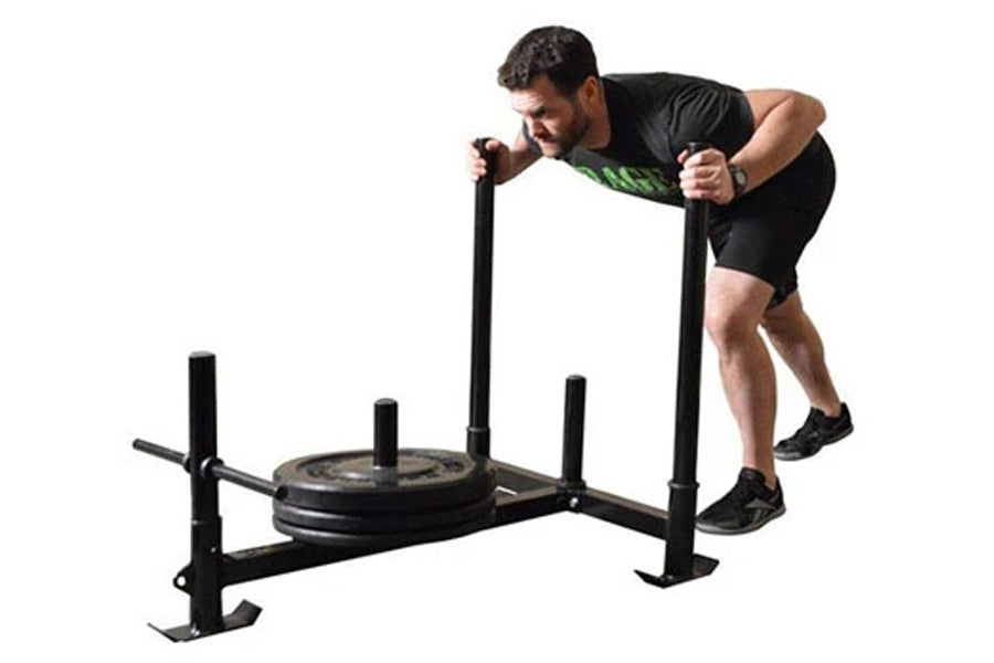 Man using black Warrior Weighted Push Sled with loaded plate, demonstrating forward push motion on white background