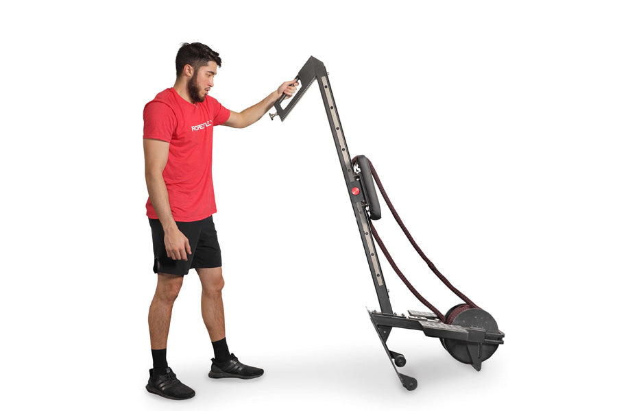 Man in red shirt and black shorts using black and gray rope rowing machine on white background