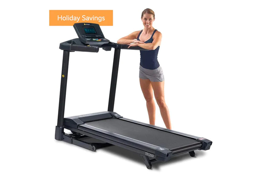 Black folding treadmill with digital console worn by model in navy tank top and gray shorts, on white background