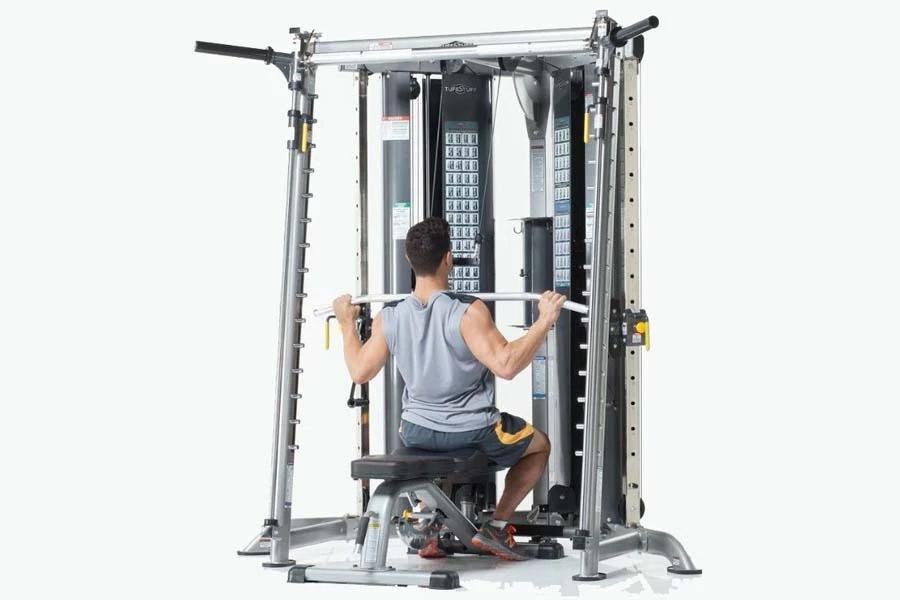 Man using silver and black multi-functional trainer with cable machine, seated on bench performing lat pulldown exercise
