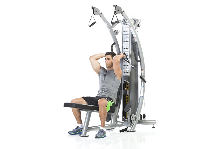 Man using silver and black dual-pulley functional trainer machine with adjustable arms and weight stack, seated on black benc