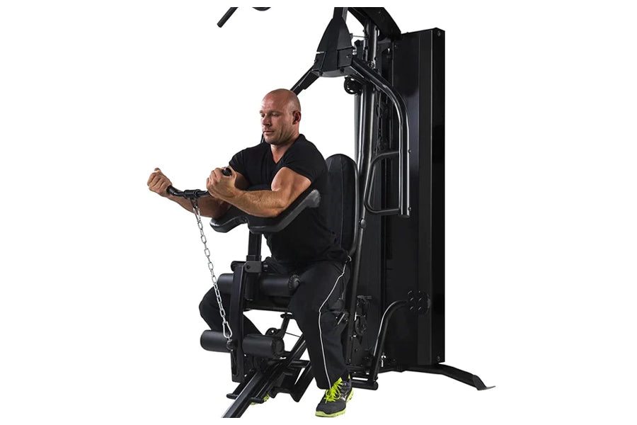 Man using black Warrior HG500 home gym with leg press and chain attachment, seated position on white background