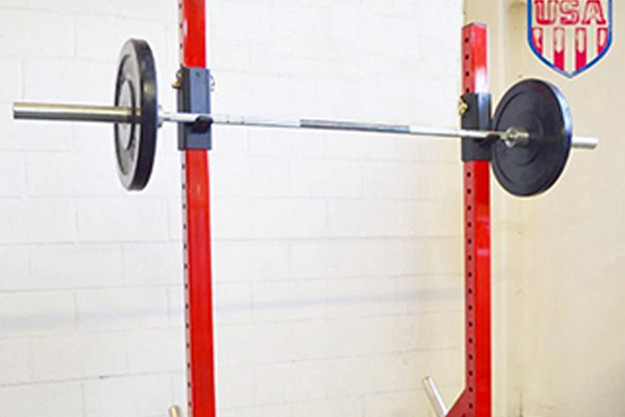 Warrior Heavy Duty Individual Squat Stands with red uprights, black weight plates, and metal bar, mounted on white brick wall
