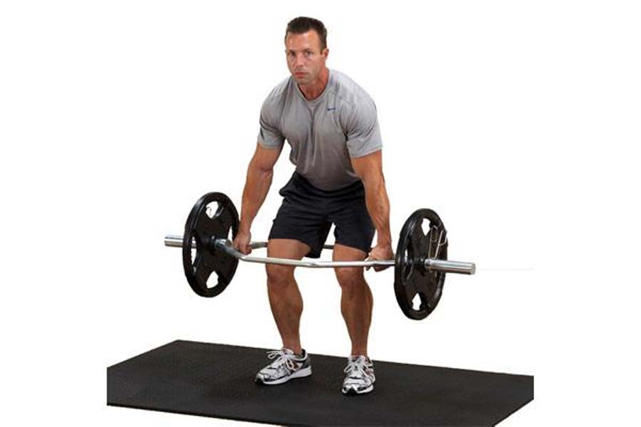 Male model wearing gray v-neck t-shirt and black shorts performing barbell deadlift with chrome hex bar on black platform