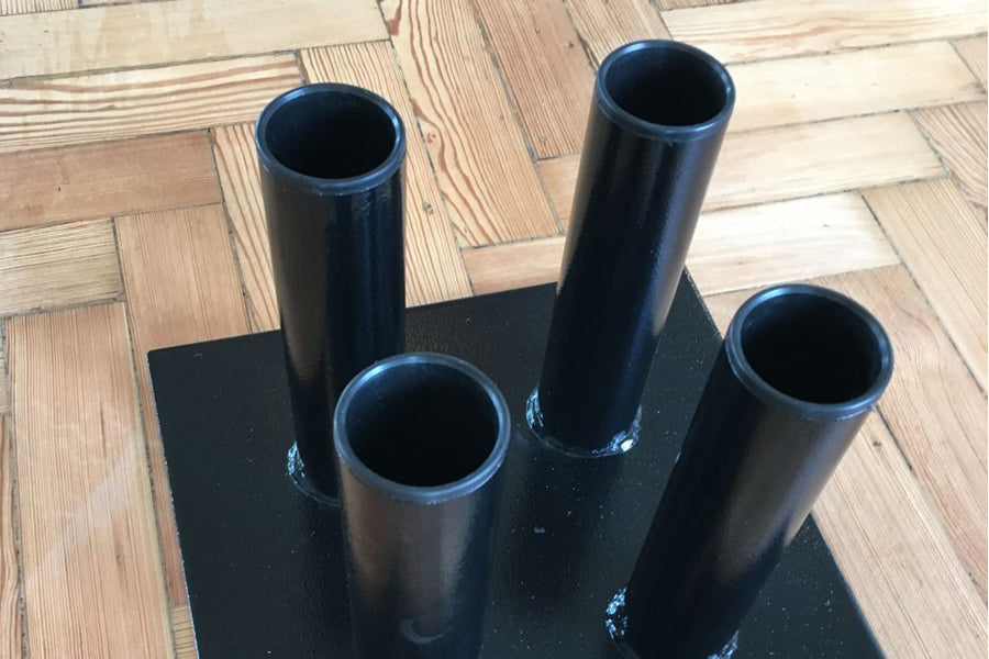 Black metal vertical bar holder with four cylindrical tubes on black base, displayed on wood floor