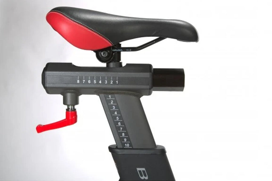 Black and red stationary exercise bike seat with resistance adjustment dial and numbered settings on white background
