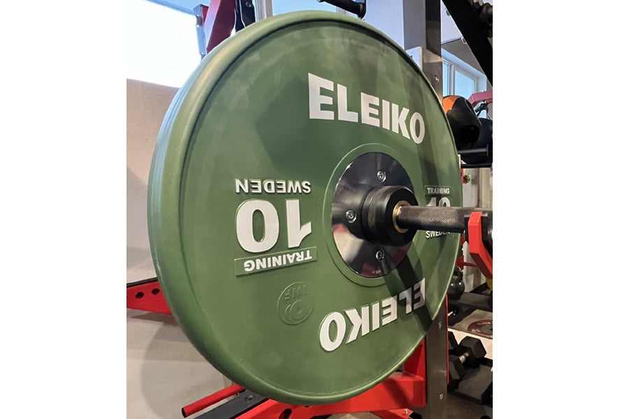 Eleiko green IWF training bumper plate 10kg mounted on red bar holder in gym setting