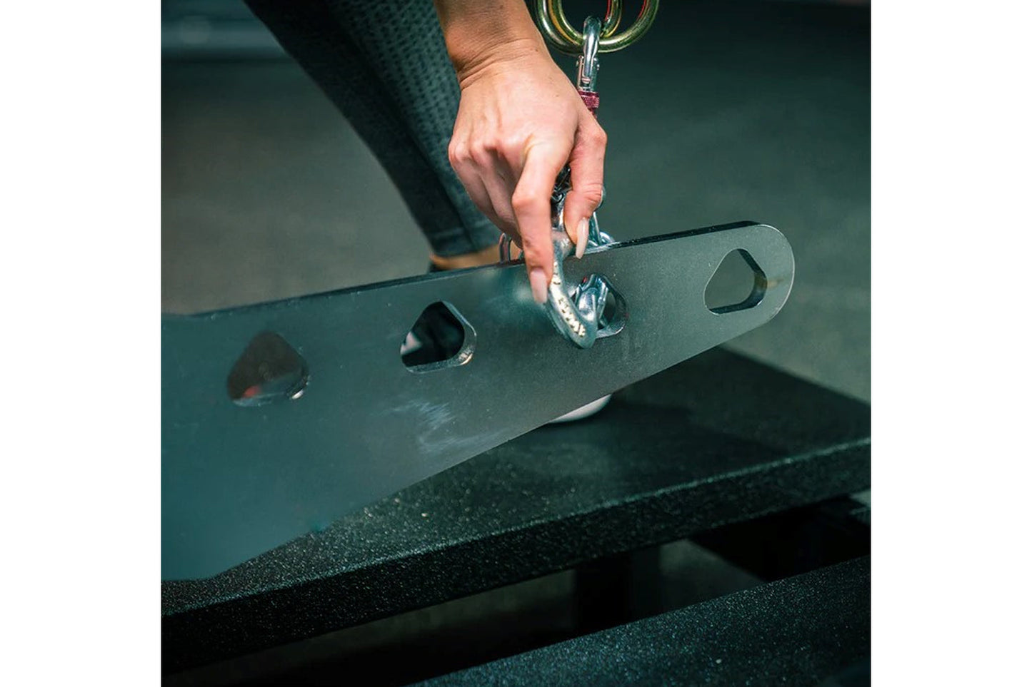 Hand attaching carabiner to dark green metal plate with multiple attachment points on fitness equipment