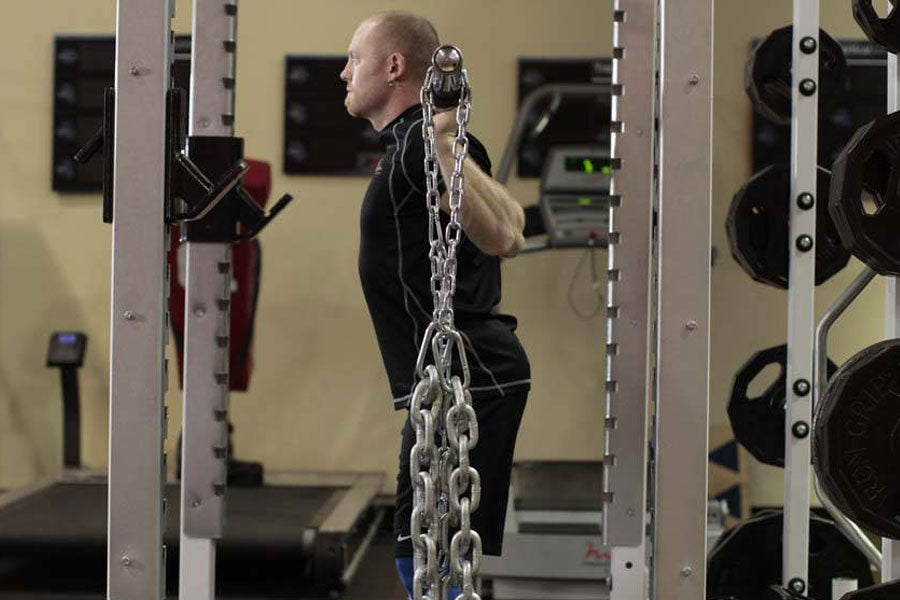 Man performing weighted exercise with heavy metal chain attached to squat rack in gym setting