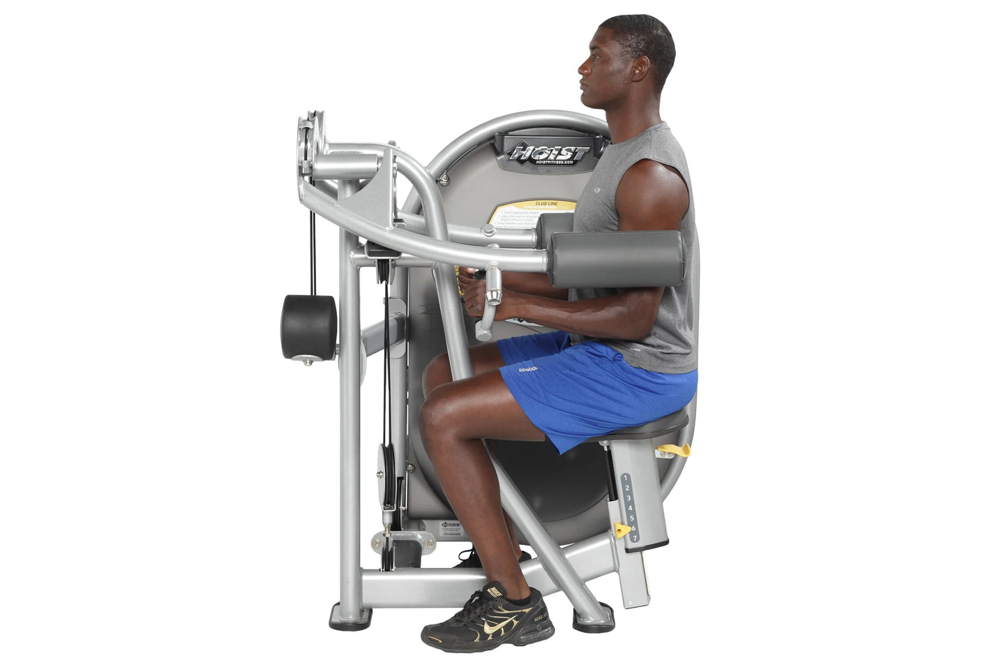 Man using silver Hoist leg press machine, wearing gray tank top and blue shorts, demonstrated on white background