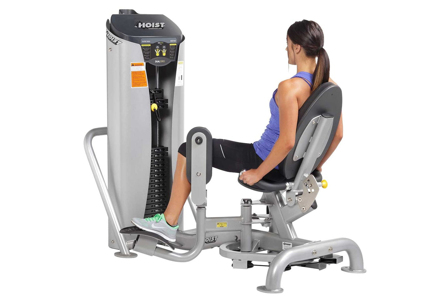 Woman using Hoist leg press machine with gray and black frame, worn by model in blue sports top on white background
