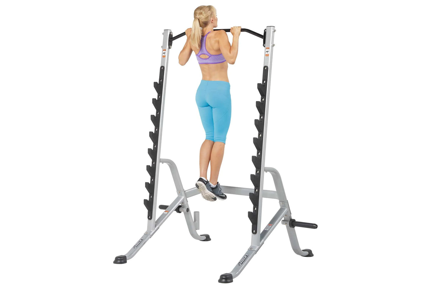 Woman using silver and black multi-purpose squat rack with adjustable barbell, worn with purple sports bra and blue capri leg