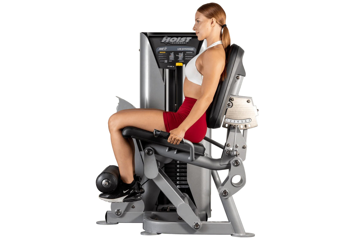 Woman using Hoist ROC-IT leg extension machine with silver frame and black seat, demonstrating proper form on white backgroun