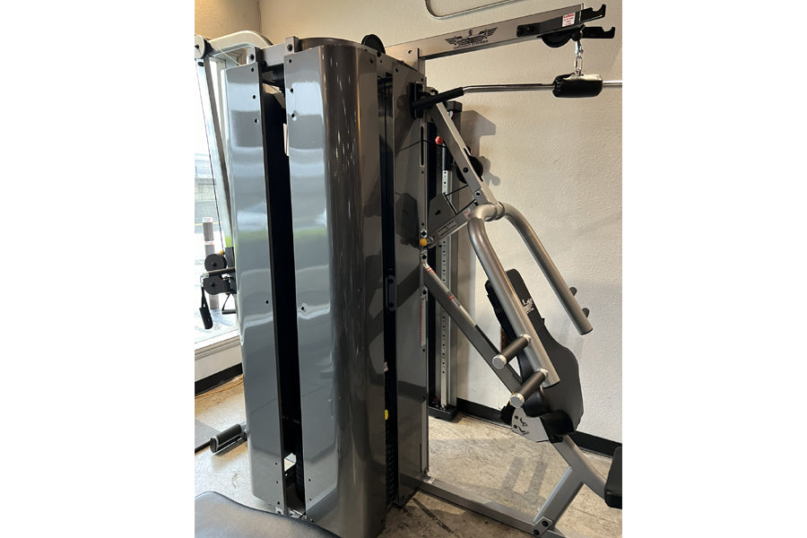 Black and gray two-stack multi-gym machine with weight stack, cables, and pulleys in showroom setting