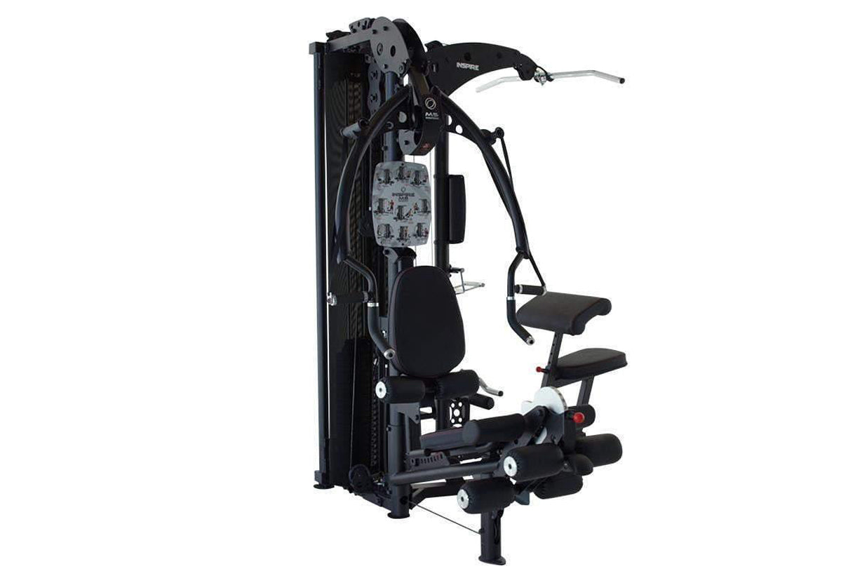 Black and white multi-gym system with padded seat, leg extension platform, chest press arm, and weight stack on white backgro
