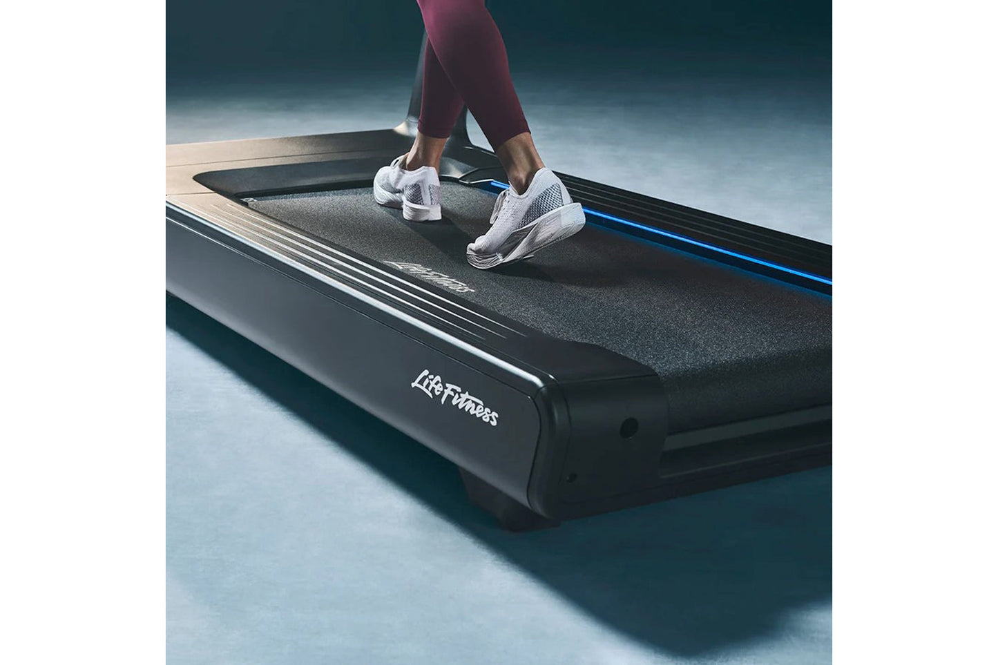 Person wearing burgundy leggings and white mesh sneakers running on Life Fitness black treadmill with blue accents