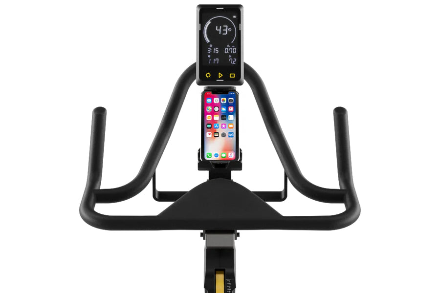Black stationary exercise bike with curved handlebars, digital display mounted above smartphone holder showing fitness metric