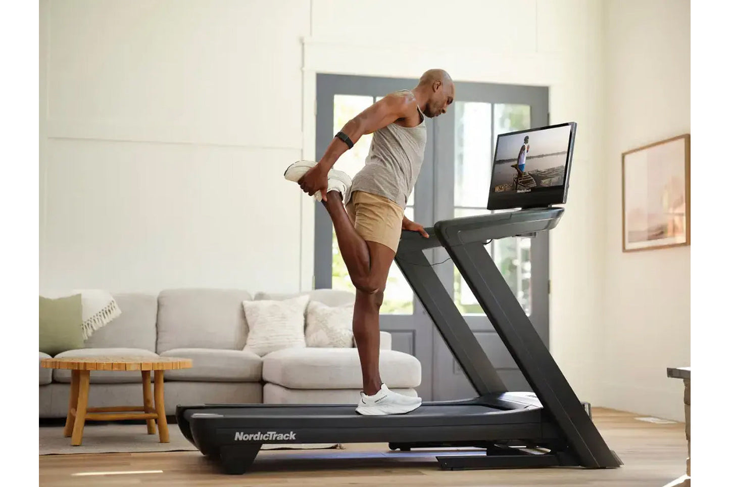Man running on black NordicTrack treadmill with built-in screen in modern living room