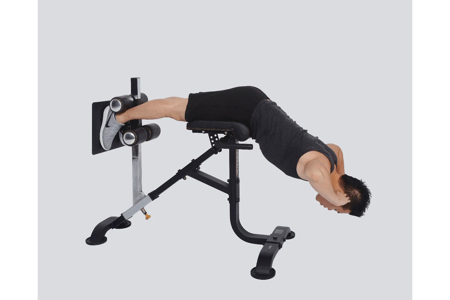 Man using black and silver hyperextension crunch machine, performing abdominal exercise on gray background