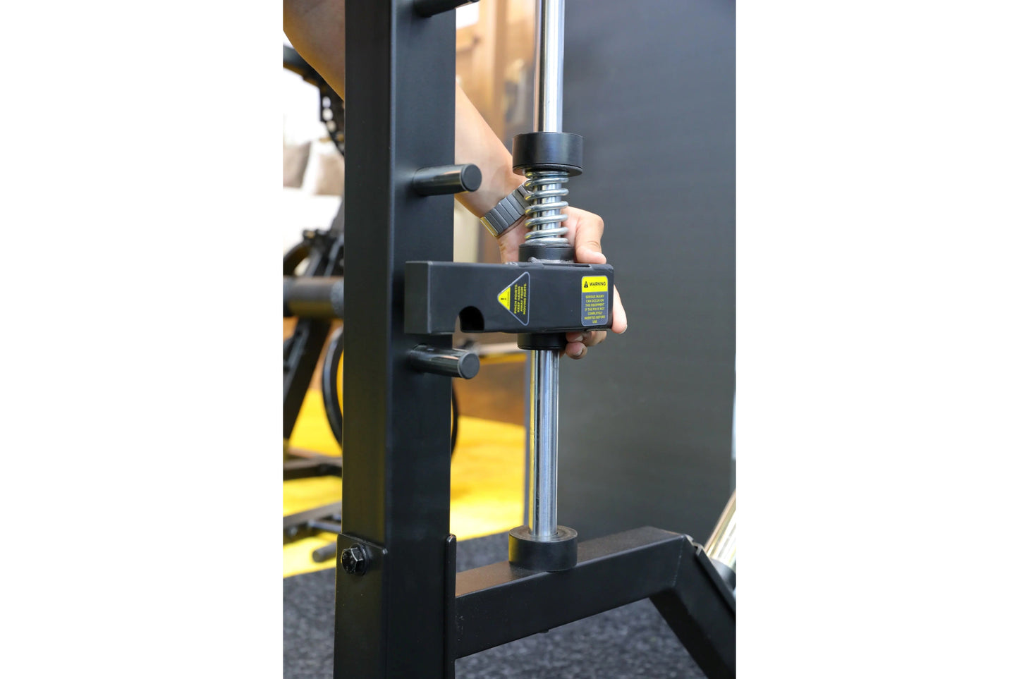 Black and yellow Smith machine with hand holding chrome linear bearing assembly during demonstration
