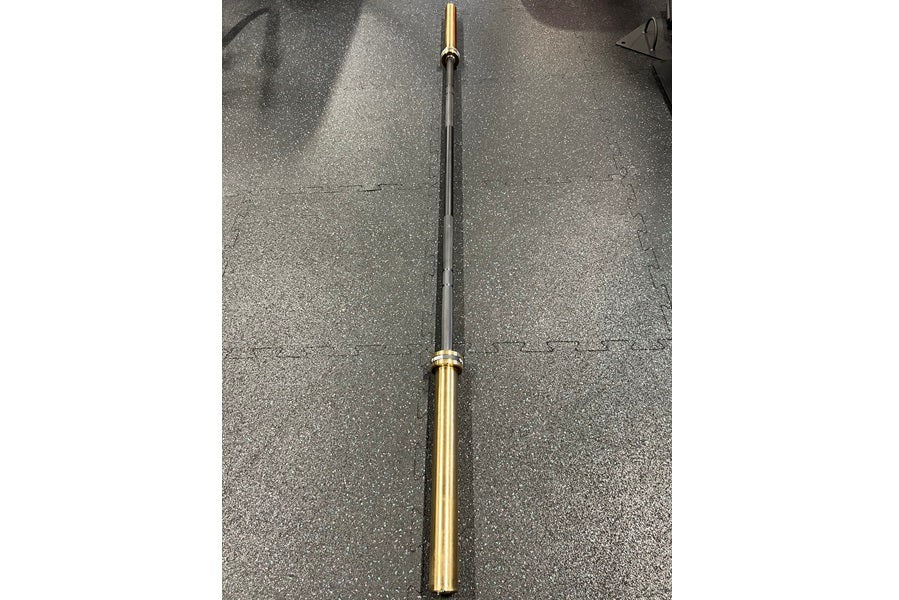 Warrior Black Cerakote and Gold Titanium Barbell with black shaft and gold sleeves, laid flat on gray background