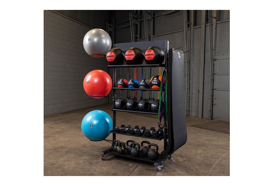 Black multi-purpose storage rack with exercise balls, medicine balls, dumbbells, and kettlebells organized on shelves in gym