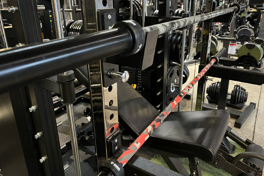 Warrior 6-bearing cerakote barbell with red camo pattern, loaded on squat rack in gym setting