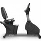 Black commercial recumbent exercise bike with padded seat, digital console, and pedal resistance system on gray base, isolate