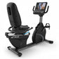 Black recumbent exercise bike with digital display console, padded seat, foot pedals, and handle grips, isolated on white bac