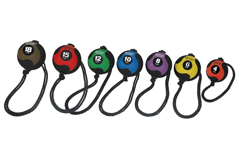 Seven medicine balls with attached rope handles in brown, red, green, blue, purple, yellow, and orange, numbered 18 to 4 poun