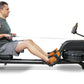 Man using black water rower with orange footrest, seated on rowing machine with display screen against white background