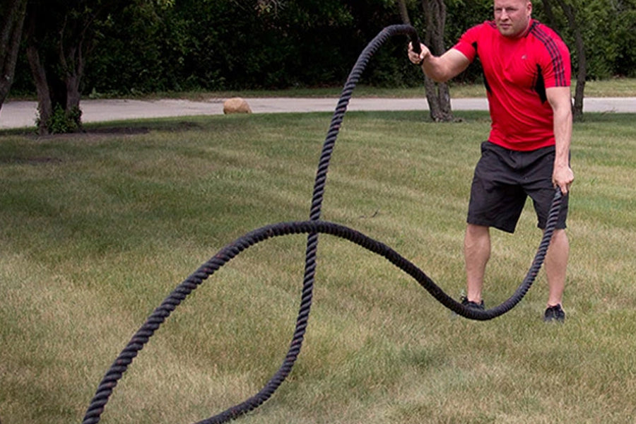 Black twisted battle ropes laid out on grass, held by man in red shirt during outdoor workout