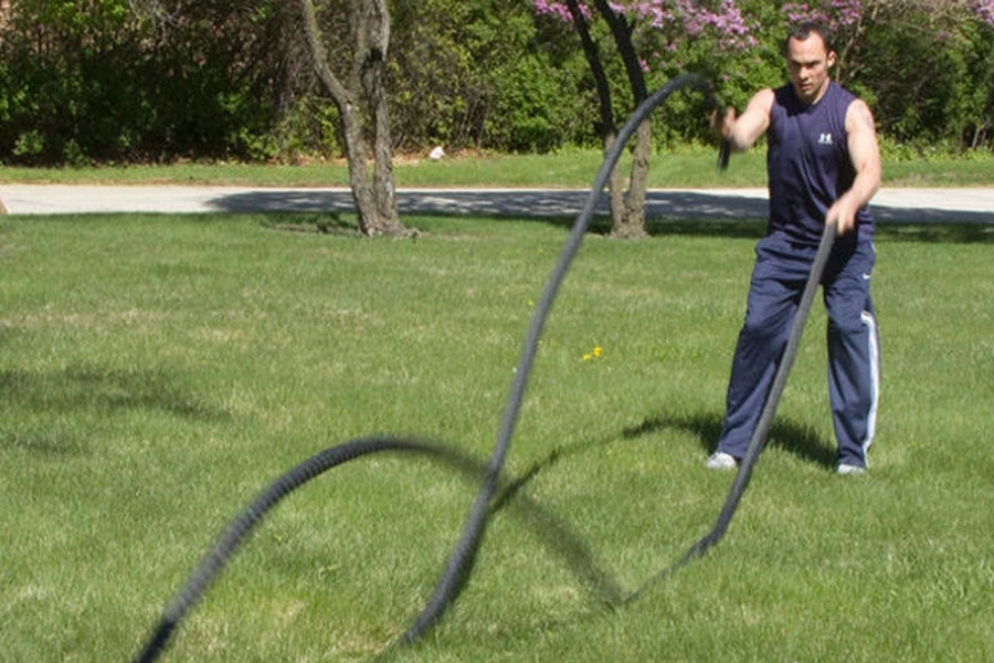 Man using black battle ropes for outdoor fitness training on grass